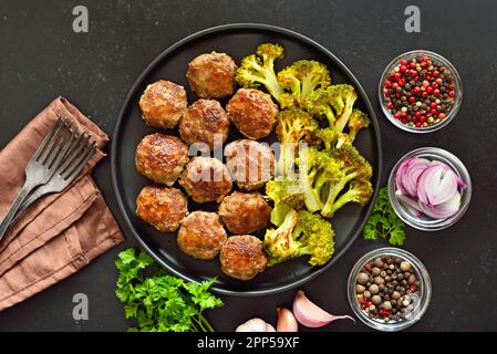 Cotolette fatte in casa e broccoli fritti sul piatto su sfondo di pietra nera. Vista dall'alto, piatto Foto Stock