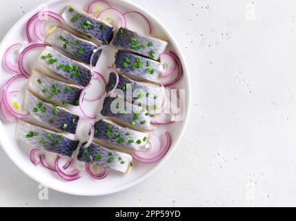 Aringa salata con cipolla su piatto su fondo di pietra bianca. Vista dall'alto, disposizione piatta Foto Stock