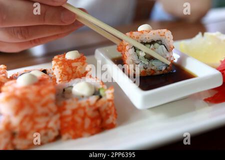 Donna che tuffa il sushi in salsa di soia nel ristorante Foto Stock
