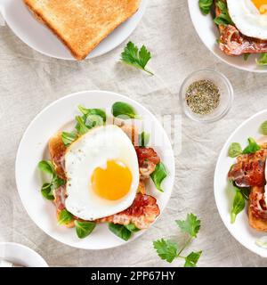 Aprire i sandwich con uova fritte, pancetta e foglie di verdure sul piatto su sfondo chiaro. Vista dall'alto, disposizione piatta Foto Stock