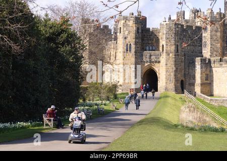 Ingresso al castello di Alnwick; con accesso per scooter per disabili; visitatori nei giardini del castello in una soleggiata giornata primaverile; Alnwick Northumberland Inghilterra Regno Unito Foto Stock