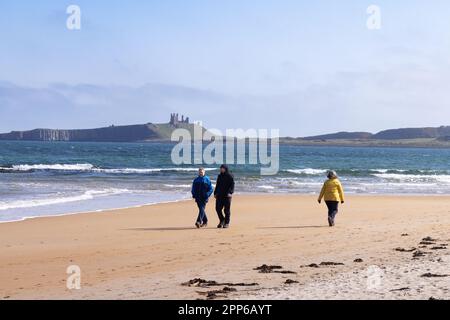 Northumberland Beach - persone che camminano sulla sabbia alla spiaggia di Embleton Bay con il castello di Dunstanburgh sullo sfondo, Northumberland UK spiaggia Foto Stock
