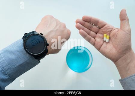 un uomo d'affari in ufficio sta guardando il suo orologio e tenendo in mano pillole gialle su uno sfondo bianco. Il concetto di farmaci tempestivi i Foto Stock