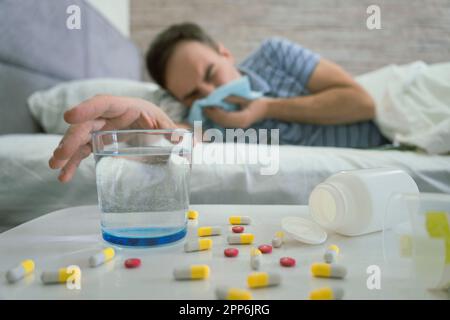 Disperato triste giovane caucasico malato maschio giace sul letto sotto coperta, soffre di runny, soffia il naso in tovagliolo in bianco camera da letto interno. Malattia, fl Foto Stock