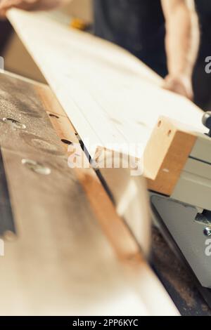 Le mani di un forte falegname tengono, guidano, trattengono, spingono e muovono il legname mentre lavora con potenti macchine da taglio nella sua officina. Le immagini trasportano stre Foto Stock