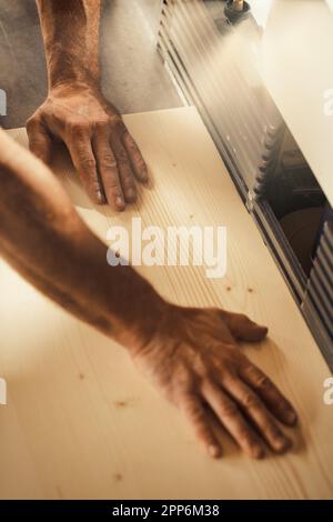 Le mani di un forte falegname tengono, guidano, trattengono, spingono e muovono il legname mentre lavora con potenti macchine da taglio nella sua officina. Le immagini trasportano stre Foto Stock