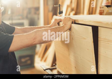 Le mani di un forte falegname tengono, guidano, trattengono, spingono e muovono il legname mentre lavora con potenti macchine da taglio nella sua officina. Le immagini trasportano stre Foto Stock