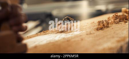 Rasatura del legno dorato a fuoco, circondata da sfocature selettive. Segatura a destra della superficie di piallatura, e un tradizionale piano a mano sul l Foto Stock