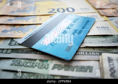 carta di pagamento su sfondo di carta dollari. la carta di credito multicurrency di plastica blu si trova su una pila di soldi euro rubli e dollari Foto Stock