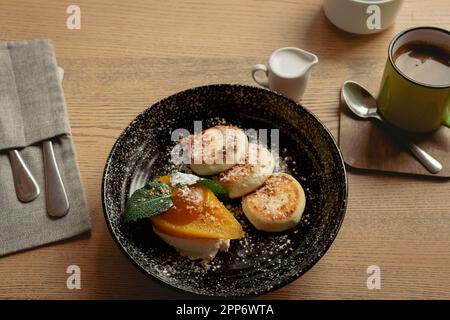 Syrniki con pera al caramello e tazza da caffè. Frittelle cagliate con caffè e latte. Colazione deliziosa. Cibo ucraino. Frittelle al formaggio e caffè. Foto Stock