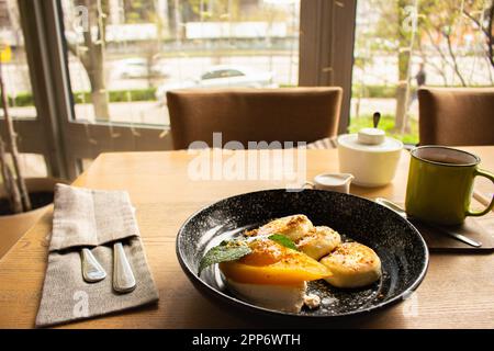 Syrniki con pera al caramello e tazza da caffè. Frittelle cagliate con caffè e latte. Deliziosa colazione al ristorante. Frittelle al formaggio e caffè. Foto Stock