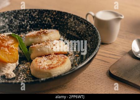 Syrniki con pera al caramello e coppa del latte. Frittelle cagliate con latte. Deliziosa colazione al ristorante. Primo piano con frittelle al formaggio. Menu del ristorante. Foto Stock