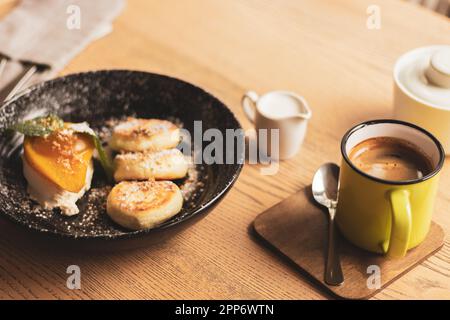 Syrniki con pera al caramello e tazza da caffè. Frittelle cagliate con caffè e latte. Colazione deliziosa. Cibo ucraino. Frittelle al formaggio e caffè. Foto Stock