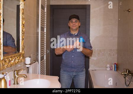 Immagine di un idraulico sorridente nel bagno di casa che tiene uno stantuffo in mano mentre si stanca un lavandino. Fai da te a casa. Foto Stock