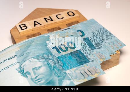 Denaro brasiliano e il simbolo della banca del Brasile in legno miniatura con l'iscrizione banco, Un sacco di banconote, banking e business concept, cl Foto Stock