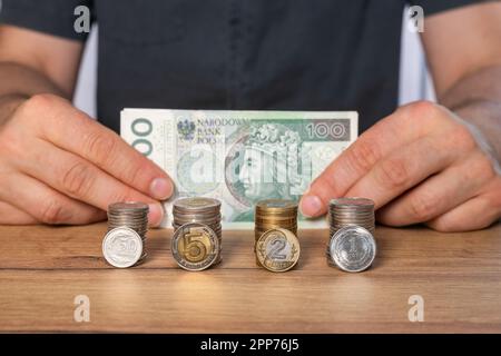 Zloty polacco, pile di monete polacche e un pacchetto di 100 banconote zloty detenute da un concetto uomo, finanziario e commerciale, risparmiando denaro Foto Stock