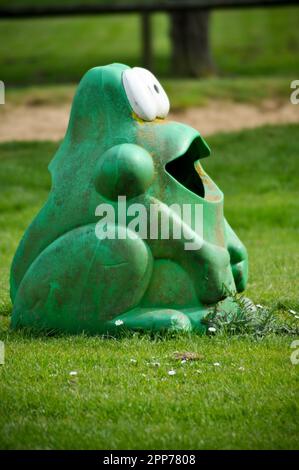 Un bidone di rifiuti in plastica a forma di rana verde, ben stagionato, in un parco giochi, Inghilterra Foto Stock