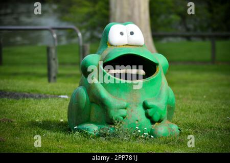 Un bidone di rifiuti in plastica a forma di rana verde, ben stagionato, in un parco giochi, Inghilterra Foto Stock