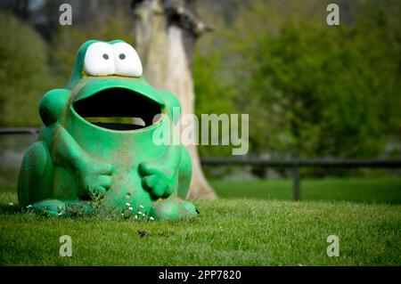 Un bidone di rifiuti in plastica a forma di rana verde, ben stagionato, in un parco giochi, Inghilterra Foto Stock