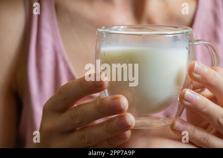 La giovane ragazza Ucraina tiene una tazza trasparente di vetro con latte al mattino Foto Stock