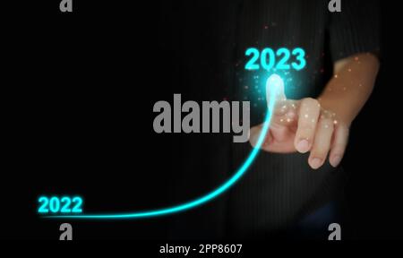 Il dito di un uomo disegna una linea curva verso l'alto da 2022 a 2023. Capodanno, Natale, start-up, nuovo business, impostare un obiettivo personale Foto Stock