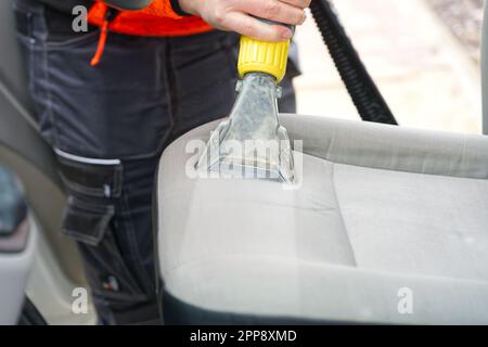 Sedile anteriore in tessuto per auto con aspirapolvere per uomo. uomo che pulisce la macchina da lavoro Foto Stock