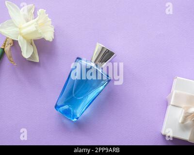 Confezione regalo bianca e bottiglia di profumo con narcoschi su fondo lilla con spazio copia. Concetto di dare un regalo alle donne, madri giorno holid Foto Stock