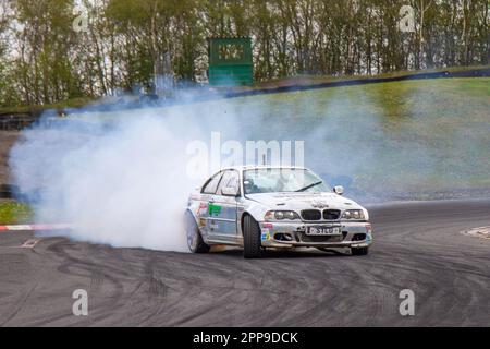 BMW auto da corsa che bruciano gomma con pneumatici che urlano a tre 3 Sisters Race Circuit a Wigan, Lancashire UK Foto Stock