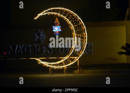 Cairo, Egitto, 17 2023 aprile: Una mezzaluna fatta di luci a LED con lampada Ramadan Fanous lanterna in strada come un segno festivo che celebra Ramadan il Foto Stock