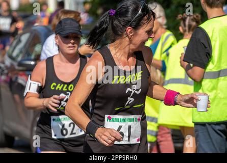 I corridori della gara di strada di Framlingham Flyers 10km prendono le tazze di plastica dell'acqua dagli assistenti Foto Stock