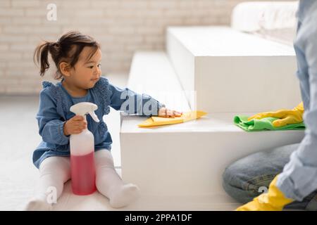 Adorabile figlia asiatica bambino aiutare la mamma a pulire camera al coperto Foto Stock