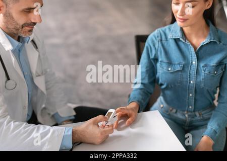 Medico di sesso maschile che misura il livello di saturazione di ossigeno per la paziente femminile mentre la donna visita terapista in clinica, ritagliato Foto Stock