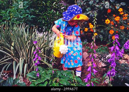 Ragazza bambino in abito floreale fiori d'acqua in giardino con un annaffiatoio di plastica Foto Stock