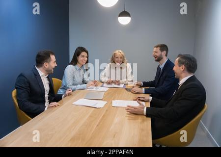 Colleghi felici e positivi che si divertono a tavola, parlano, ridono Foto Stock
