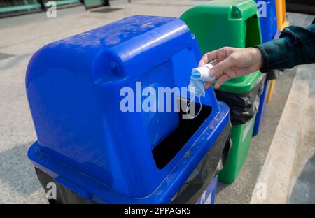 Rifiuti medici. Persone mano gettando usato medico maschera di protezione del viso nel cestino. Cestino in plastica blu. Uomo gettare la maschera usata nel cestino. Foto Stock