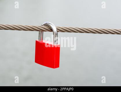 Primo piano di un lucchetto rosso appeso su un cavo di acciaio Foto Stock