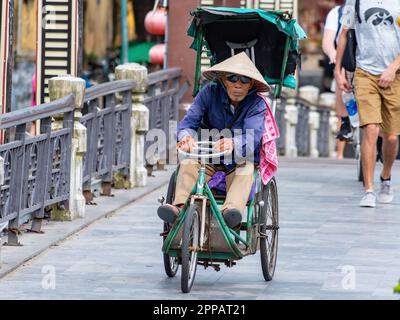 Uomo anziano e disabile che attraversa un ponte sul triciclo a mano a Hoi An, provincia di Quang Nam, Vietnam di notte. La città vecchia di Hoi An è un worl Foto Stock