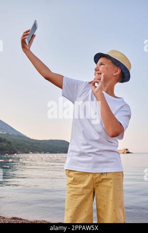 Ragazzo in cappello porta un ritratto selfie vicino al mare. Felice ragazzo godendo vacanze estive in spiaggia Foto Stock