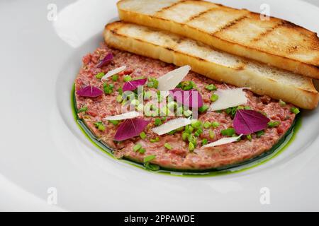 Tartaro di carne, con cipollotti, e pane tostato, su un piatto, su uno sfondo scuro Foto Stock