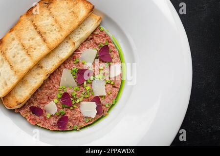 Tartaro di carne, con cipollotti, e pane tostato, su un piatto, su uno sfondo scuro Foto Stock