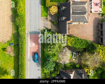 Vista dall'alto del drone di una segnaletica stradale lenta vista su una pericolosa strada rurale inglese. Una sola auto passa ad alta velocità. Foto Stock