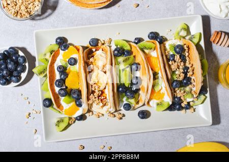 Pancake Taco con frutta fresca, ripieno di mirtillo e yogurt, colazione sana o snack su sfondo luminoso Foto Stock