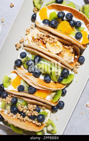 Pancake Taco con frutta fresca, ripieno di mirtillo e yogurt, colazione sana o snack su sfondo luminoso Foto Stock