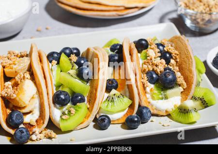 Pancake Taco con frutta fresca, ripieno di mirtillo e yogurt, colazione sana o snack su sfondo luminoso Foto Stock
