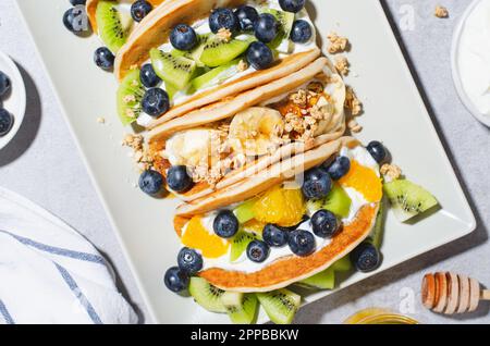 Pancake Taco con frutta fresca, ripieno di mirtillo e yogurt, colazione sana o snack su sfondo luminoso Foto Stock