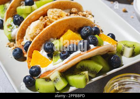 Pancake Taco con frutta fresca, ripieno di mirtillo e yogurt, colazione sana o snack su sfondo luminoso Foto Stock