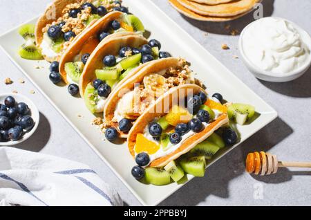 Pancake Taco con frutta fresca, ripieno di mirtillo e yogurt, colazione sana o snack su sfondo luminoso Foto Stock