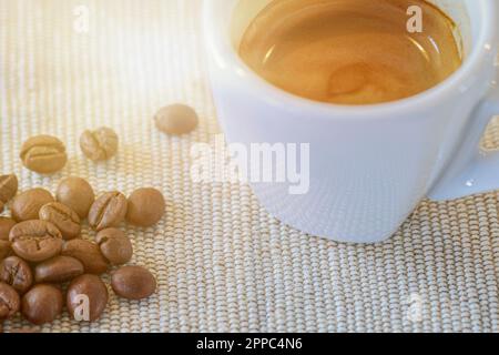 Eine gefüllte espresso Tasse steht neben Kaffeeeebohnen auf einem Tisch Foto Stock