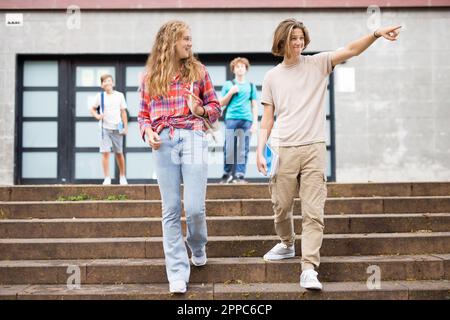 Gli studenti escono dalle porte dell'università. Il ragazzo punta la mano a qualcuno Foto Stock