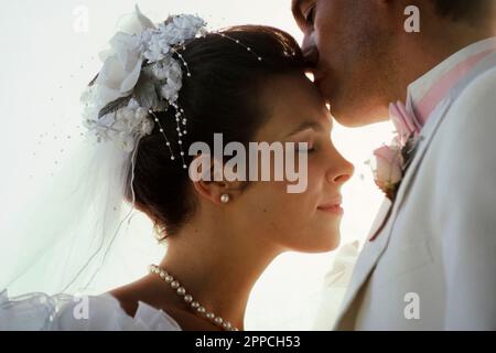 Appena sposato, il nuovo marito caucasico bacia la sua bella giovane moglie sulla fronte Foto Stock